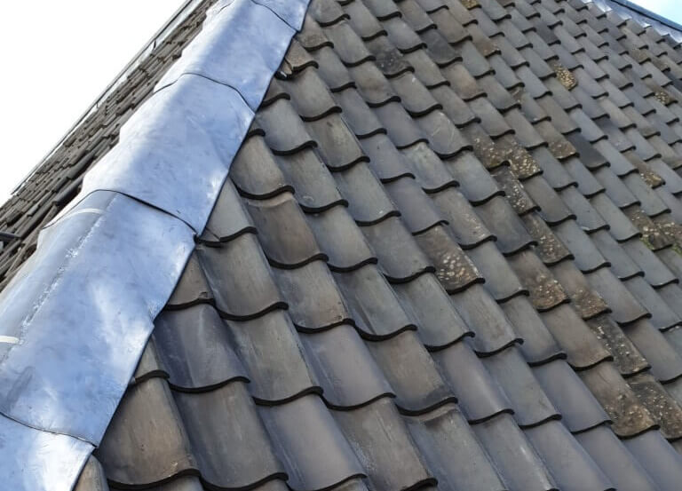 Op de foto zie ik een hellend pannendak waarbij langs de nok verse loodslabben strak zijn aangebracht. Dit past bij een dakdekkersdienst voor renovatie en waterdichte afwerking van hellende daken. Het hoofddoel van deze dienst is om het dak duurzaam en volledig waterdicht te maken. De loodslabben zijn nauwkeurig op maat gesneden voor een perfecte aansluiting, het gebruikte materiaal is UV- en weerbestendig voor langdurige bescherming en de afwerking is direct inzetbaar zonder extra herstelwerkzaamheden.